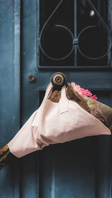 A person wearing a floral-patterned sleeve is holding a bouquet of fresh flowers wrapped in light pink paper, delivering it through a dark blue door with a decorative black iron grille above the door 